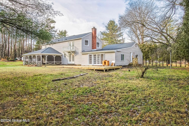 back of house featuring a yard, a balcony, a wooden deck, and a sunroom