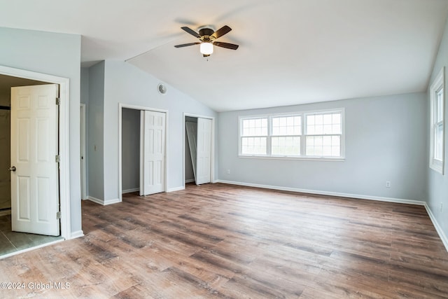 unfurnished bedroom featuring multiple closets, ceiling fan, vaulted ceiling, and hardwood / wood-style flooring