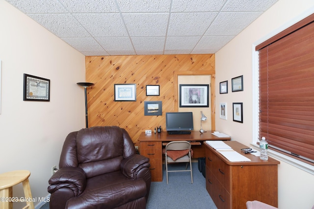 carpeted home office with wooden walls and a drop ceiling