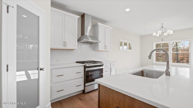 kitchen featuring sink, wall chimney exhaust hood, stainless steel range with gas cooktop, hardwood / wood-style floors, and white cabinets