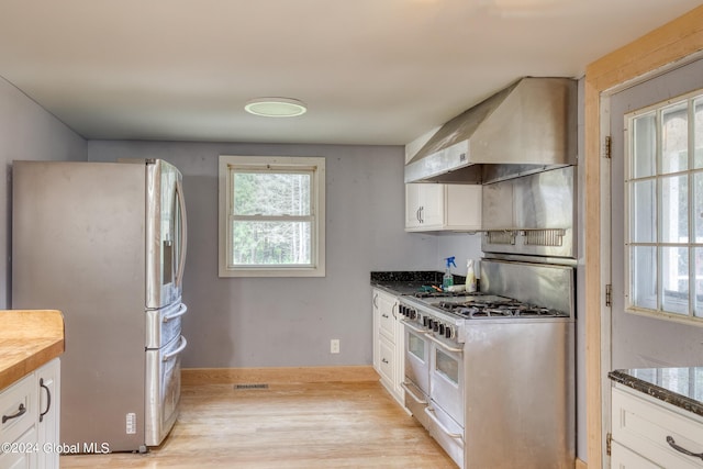 kitchen with wall chimney exhaust hood, dark stone counters, light hardwood / wood-style floors, white cabinets, and appliances with stainless steel finishes