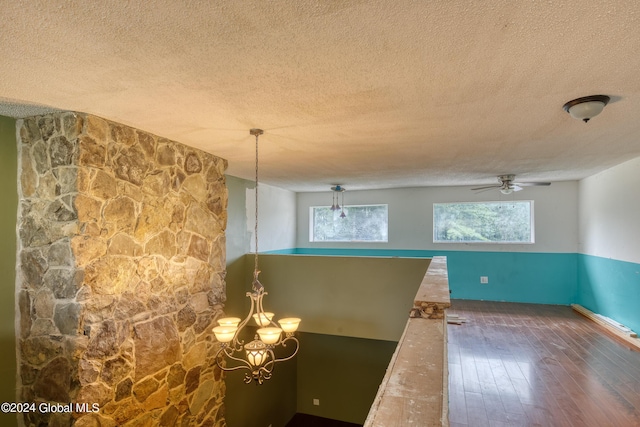 spare room with ceiling fan with notable chandelier, dark hardwood / wood-style flooring, and a textured ceiling