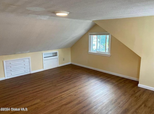 additional living space with a textured ceiling, lofted ceiling, and dark wood-type flooring