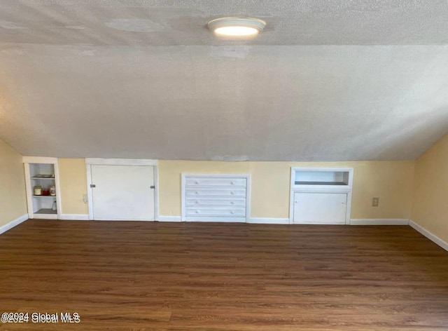 bonus room with built in shelves, lofted ceiling, a textured ceiling, and dark wood-type flooring