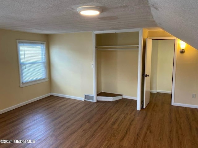 unfurnished bedroom featuring vaulted ceiling, dark wood-type flooring, and a textured ceiling