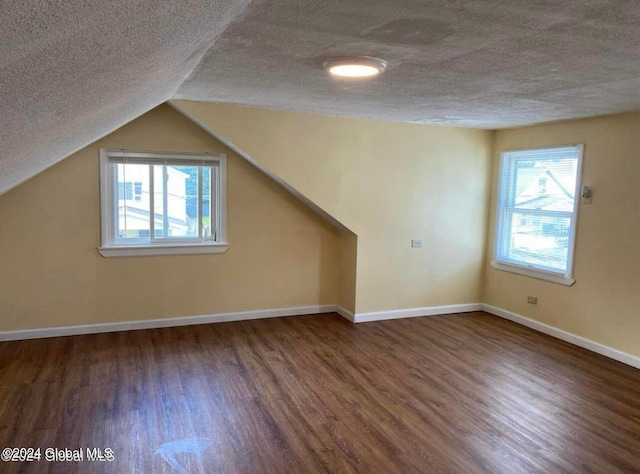 additional living space with a textured ceiling, dark hardwood / wood-style flooring, and vaulted ceiling