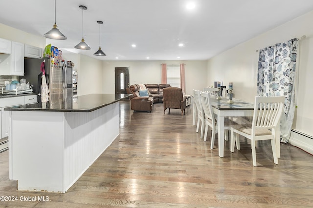 kitchen with stainless steel refrigerator, white cabinetry, wood-type flooring, decorative light fixtures, and a kitchen island