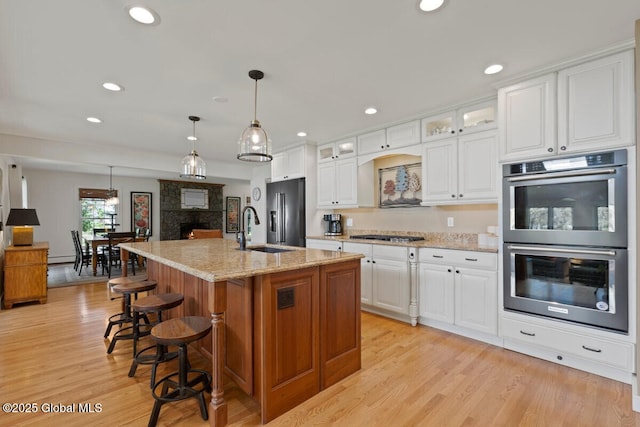 kitchen with light stone countertops, sink, stainless steel appliances, an island with sink, and white cabinets