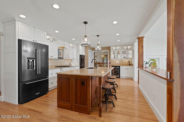 kitchen with wine cooler, white cabinetry, high end fridge, and a center island with sink