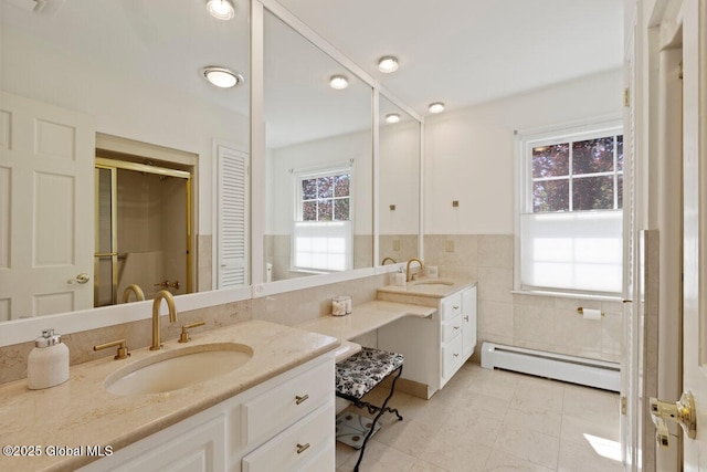 bathroom with vanity, plenty of natural light, baseboard heating, and tile walls