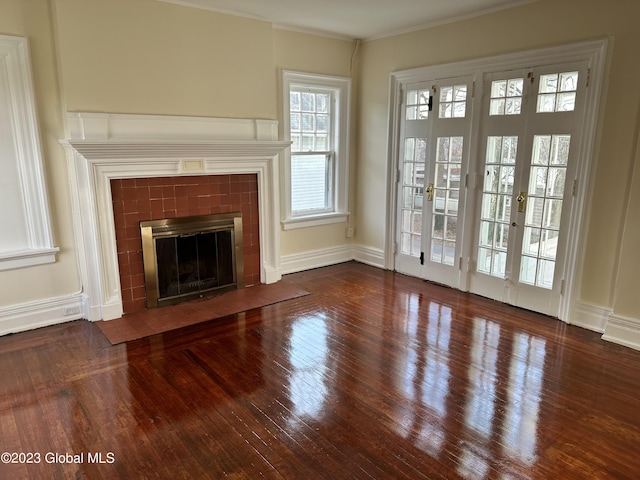 unfurnished living room featuring ornamental molding, a tiled fireplace, dark wood-type flooring, and french doors