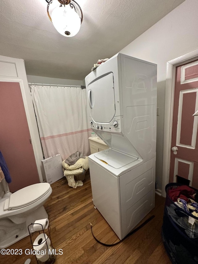 bathroom with a textured ceiling, hardwood / wood-style floors, stacked washer and clothes dryer, and toilet