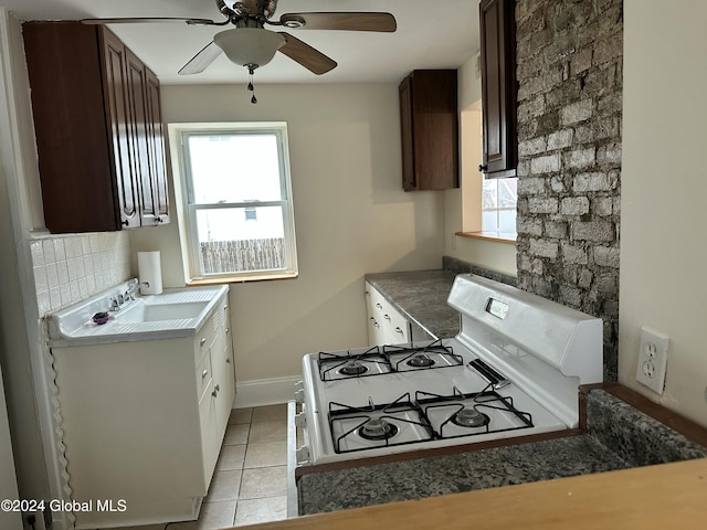 kitchen featuring dark brown cabinets, ceiling fan, sink, light tile patterned floors, and white gas stove