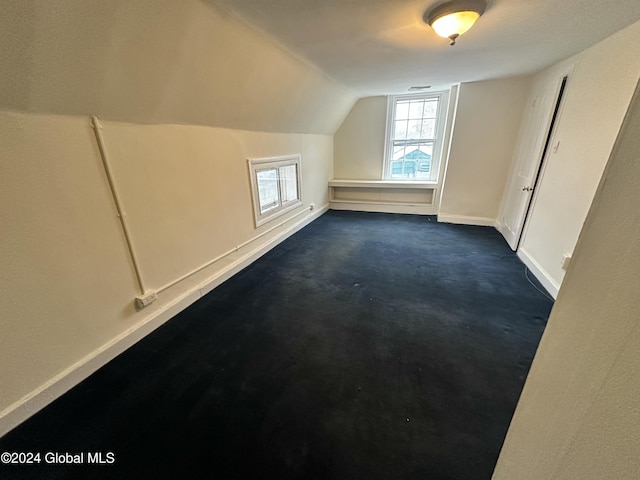 additional living space with vaulted ceiling and dark colored carpet