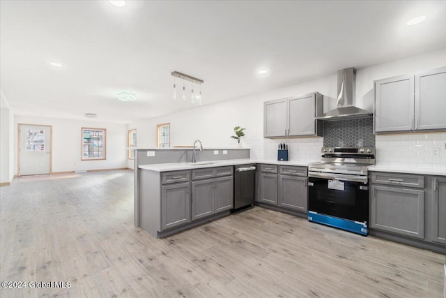 kitchen with gray cabinetry, decorative backsplash, appliances with stainless steel finishes, wall chimney exhaust hood, and a sink