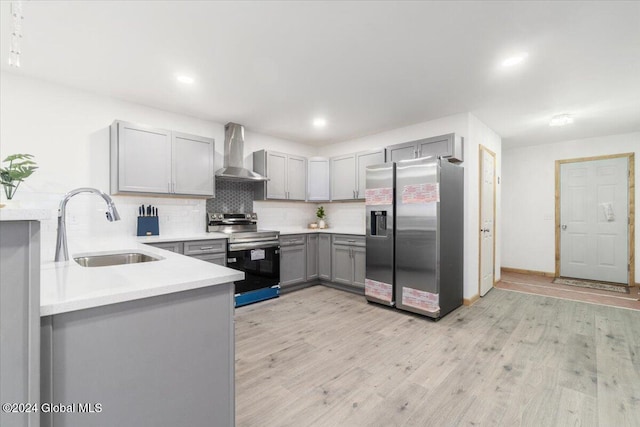 kitchen featuring light wood-type flooring, gray cabinets, stainless steel appliances, wall chimney exhaust hood, and a sink