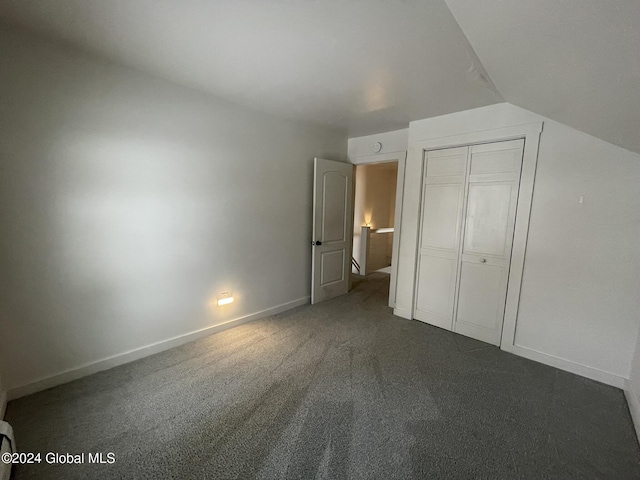 unfurnished bedroom featuring dark colored carpet, lofted ceiling, and a closet