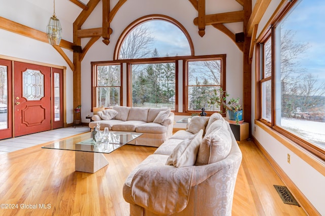 living room featuring a notable chandelier, light hardwood / wood-style floors, beam ceiling, and high vaulted ceiling