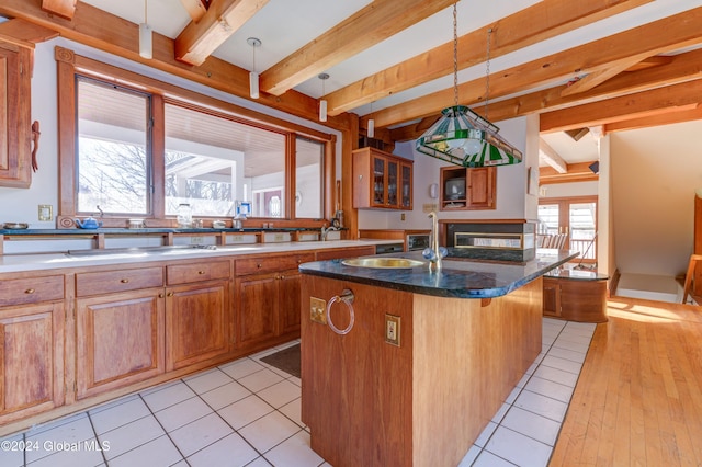 kitchen featuring a breakfast bar, a kitchen island with sink, hanging light fixtures, light wood-type flooring, and beam ceiling