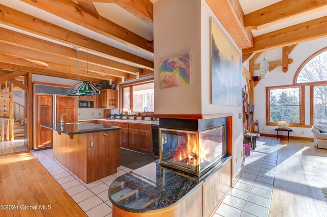 kitchen with light wood-type flooring, black appliances, a center island with sink, beamed ceiling, and a breakfast bar area