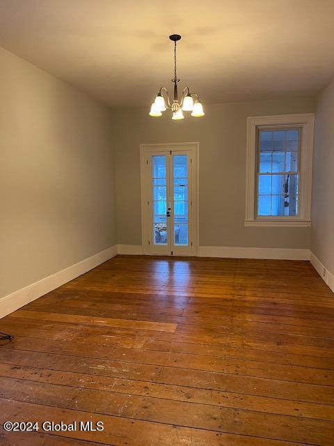 spare room with wood-type flooring, french doors, and an inviting chandelier