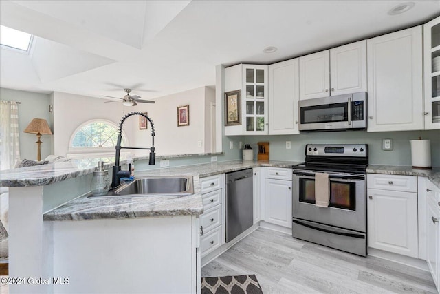 kitchen featuring kitchen peninsula, a skylight, appliances with stainless steel finishes, light hardwood / wood-style floors, and white cabinetry