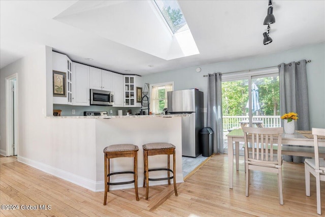 kitchen with track lighting, a skylight, light hardwood / wood-style floors, white cabinetry, and stainless steel appliances