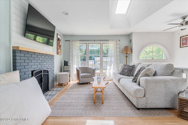 living room with ceiling fan, a skylight, a fireplace, and light hardwood / wood-style flooring