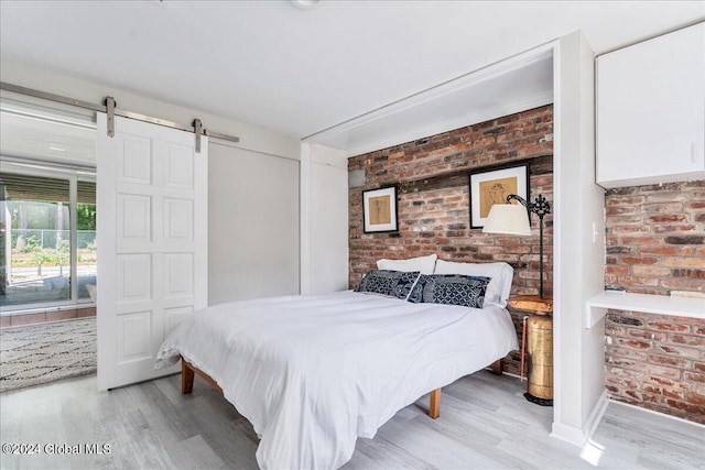 bedroom with a barn door, light wood-type flooring, and brick wall