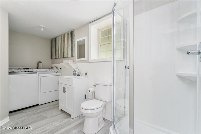 bathroom featuring vanity, a shower with door, washer and dryer, hardwood / wood-style floors, and toilet