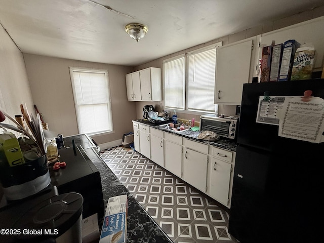 kitchen featuring a toaster, dark countertops, freestanding refrigerator, white cabinetry, and a sink