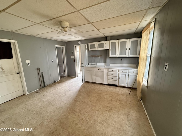 kitchen featuring a paneled ceiling, glass insert cabinets, light countertops, a ceiling fan, and white cabinets