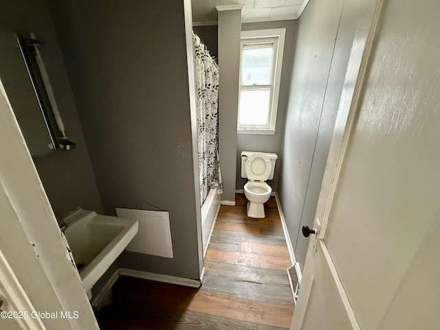 bathroom featuring a shower with shower curtain, baseboards, crown molding, toilet, and wood finished floors