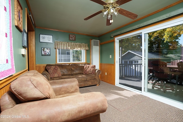 carpeted living room featuring ceiling fan, crown molding, and wood walls