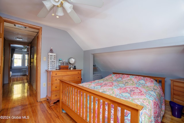 bedroom featuring ceiling fan, light wood-type flooring, radiator heating unit, and vaulted ceiling