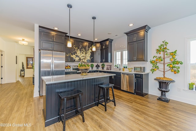 kitchen featuring a breakfast bar, hanging light fixtures, light hardwood / wood-style floors, a kitchen island, and stainless steel appliances
