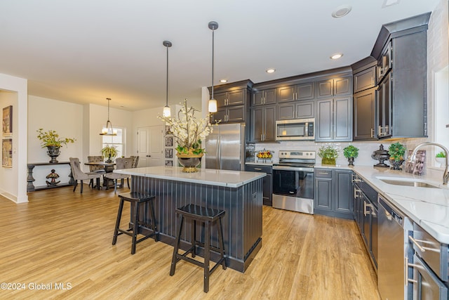 kitchen featuring light wood-type flooring, stainless steel appliances, sink, decorative light fixtures, and a kitchen island