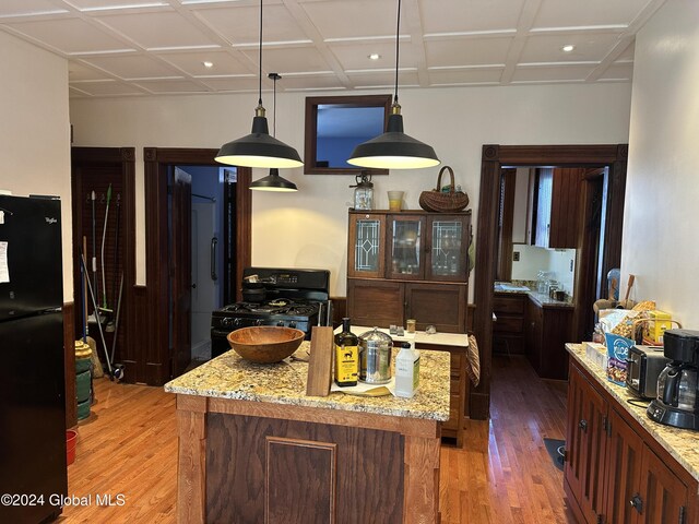 kitchen with black appliances, light wood-style flooring, light stone countertops, and a center island