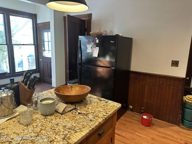 kitchen with light stone counters, a wainscoted wall, freestanding refrigerator, light wood-style floors, and wood walls