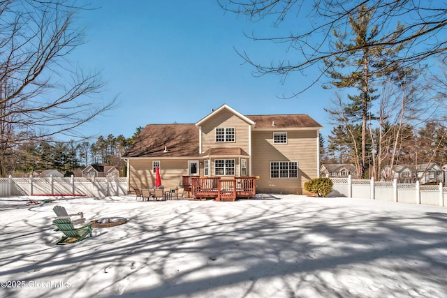 snow covered back of property with a deck, an outdoor fire pit, and a fenced backyard