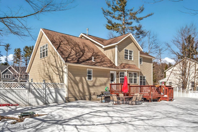 snow covered house featuring a deck, fence, and a shingled roof