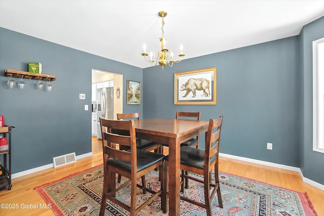 dining area with light wood-style floors, visible vents, a chandelier, and baseboards