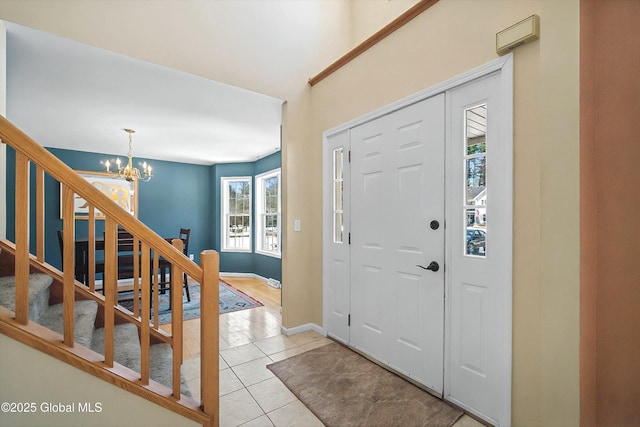 foyer entrance featuring light tile patterned flooring, stairway, a chandelier, and baseboards