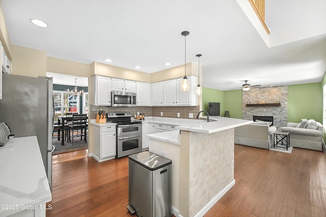 kitchen with dark wood-style floors, a peninsula, a fireplace, appliances with stainless steel finishes, and open floor plan