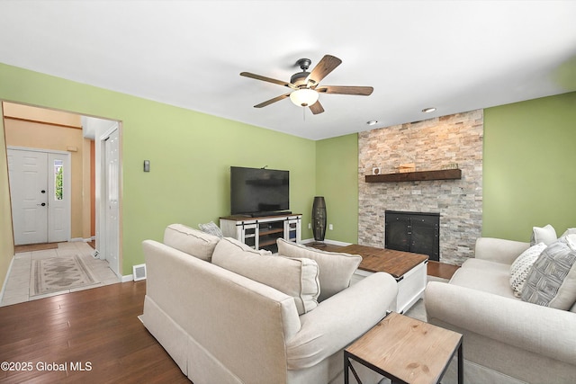 living area featuring wood finished floors, visible vents, baseboards, ceiling fan, and a stone fireplace