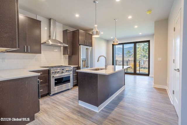 kitchen featuring high quality appliances, light countertops, wall chimney exhaust hood, an island with sink, and decorative light fixtures