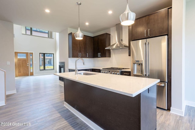 kitchen featuring decorative light fixtures, high end fridge, a sink, dark brown cabinetry, and wall chimney exhaust hood