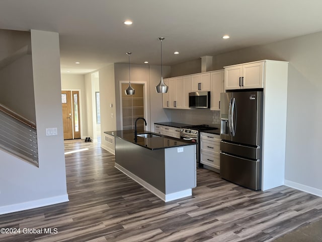 kitchen with decorative light fixtures, white cabinets, appliances with stainless steel finishes, dark countertops, and a center island with sink