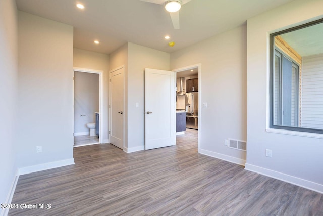 unfurnished bedroom featuring dark wood-style floors, baseboards, high end refrigerator, and visible vents