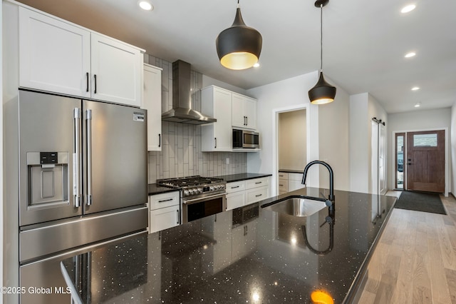 kitchen with white cabinets, premium appliances, wall chimney exhaust hood, hanging light fixtures, and a sink